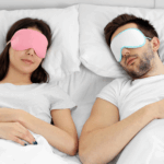 Man en vrouw slapen rustig in bed met een roze en wit slaapmasker voor volledige verduistering.