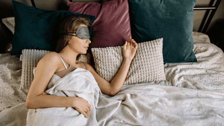 Vrouw in bed met een grijs slaapmasker van zijde voor verduistering en bescherming van de gevoelige huid.