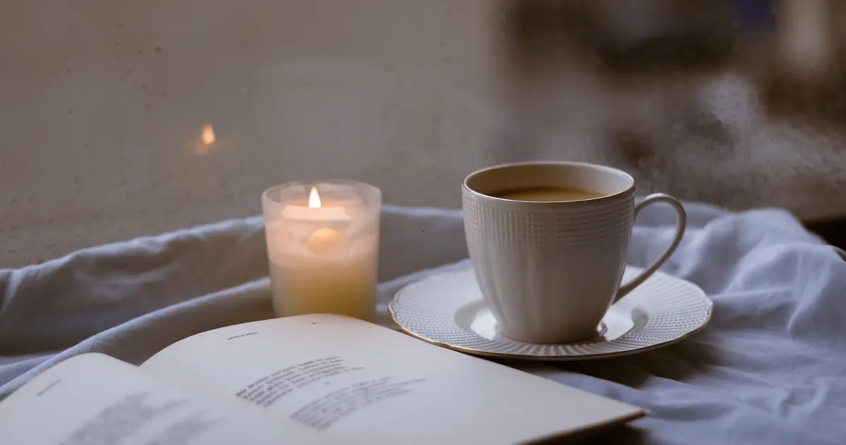 Een rustgevende avondroutine met een kop thee, een open boek en een kaars om spanning los te laten voor het slapen.